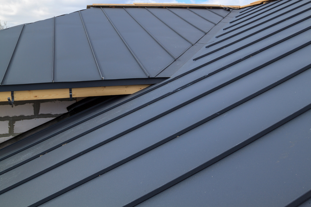 A close-up view of a dark gray metal roofing system with standing seam panels and visible wooden beams at the edge.