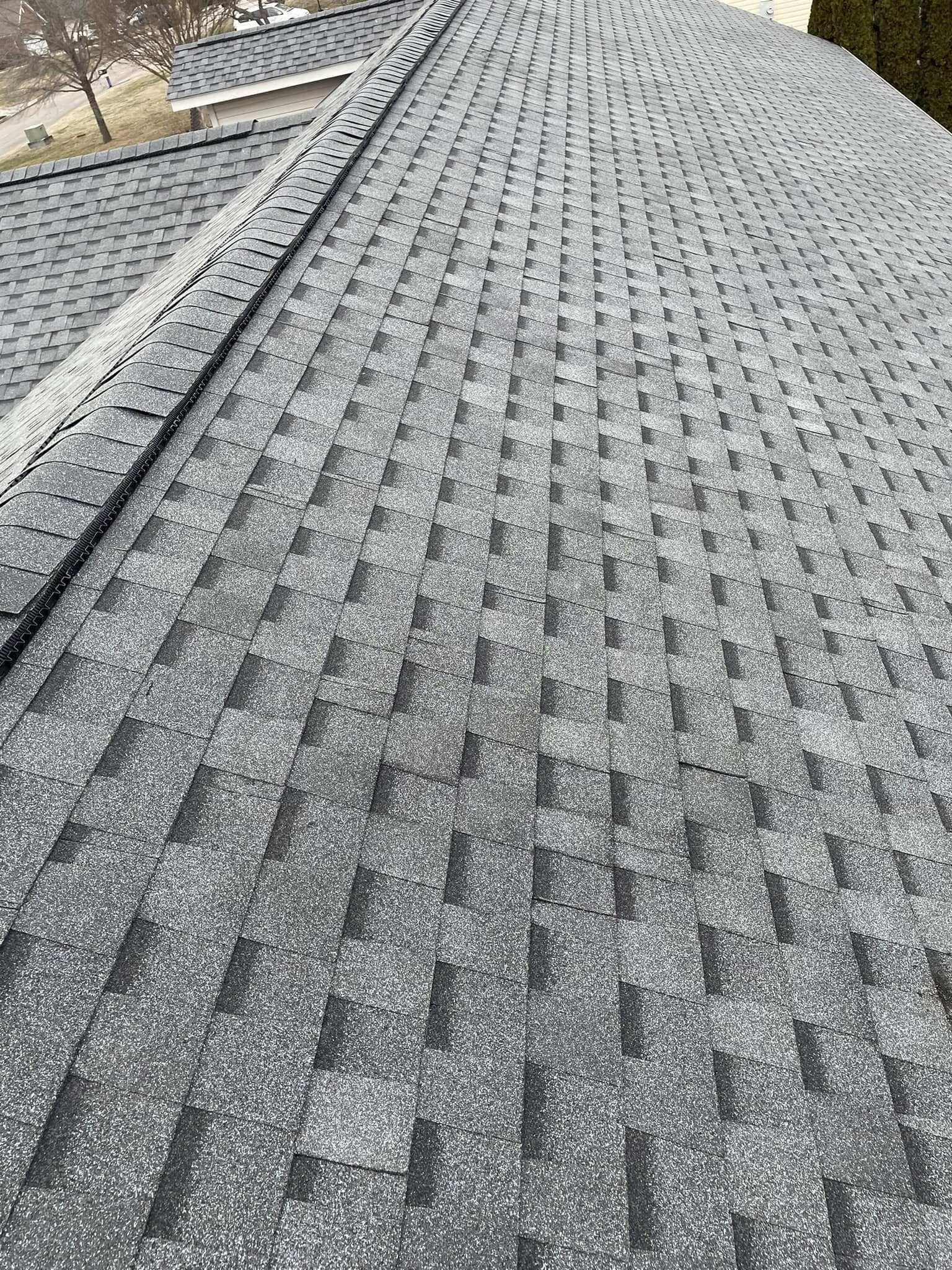 A close-up view of a gray asphalt shingle roof with a ridge line, showing uniform installation and no visible damage.