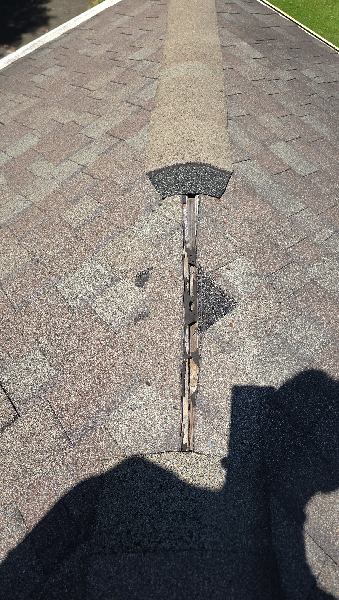A roof ridge vent with damaged and exposed wood underneath the shingles, showing signs of wear and potential need for repair.